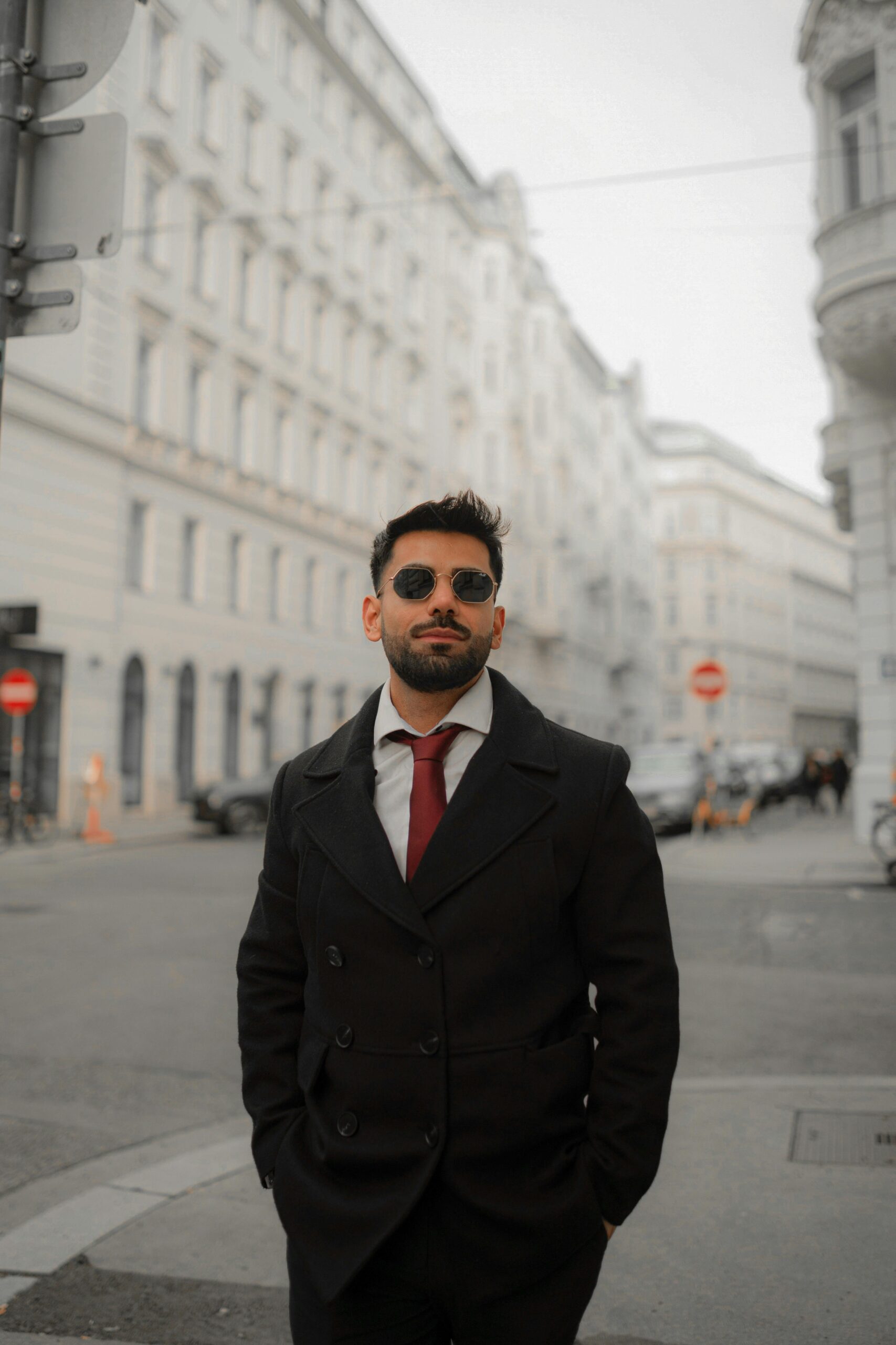 Man in black coat and sunglasses walking in a European city street.